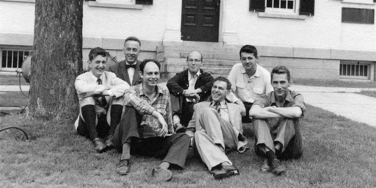 A black-and-white photograph of seven participants in the 1956 Dartmouth workshop, seated outside Dartmouth Hall.